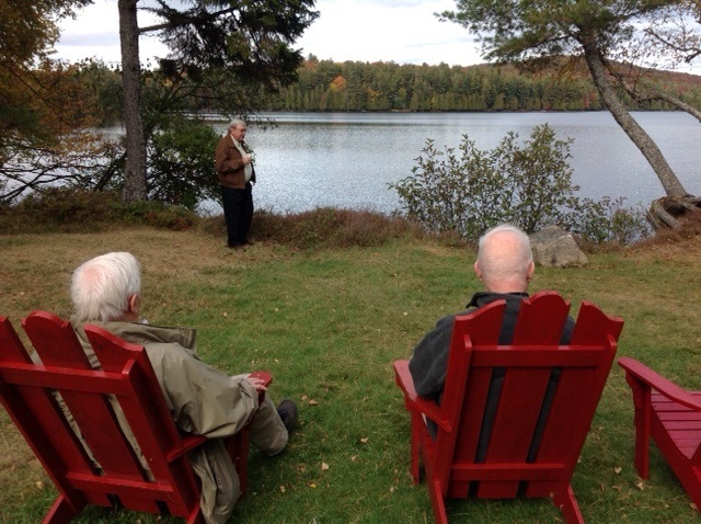 2 men in red chairs looking over sagamore and one man standing near lake